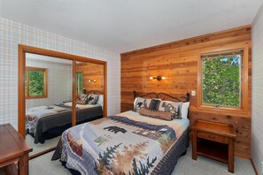 Ein Schlafzimmer mit einem großen Bett, einem Nachttisch, einem Spiegel und einem Fenster mit Blick auf Grünflächen.
