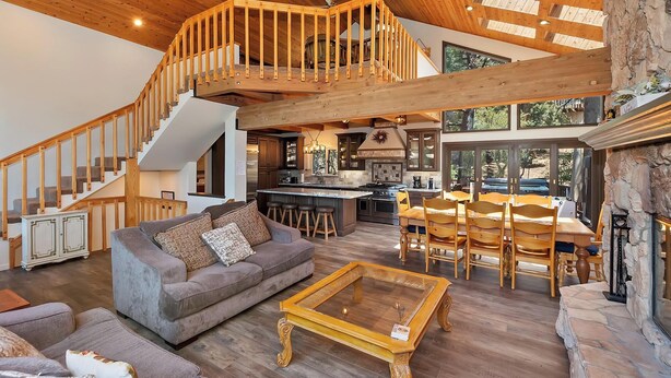 Amplia sala de estar con techo alto, escalera de madera, chimenea y cocina con una isla grande.