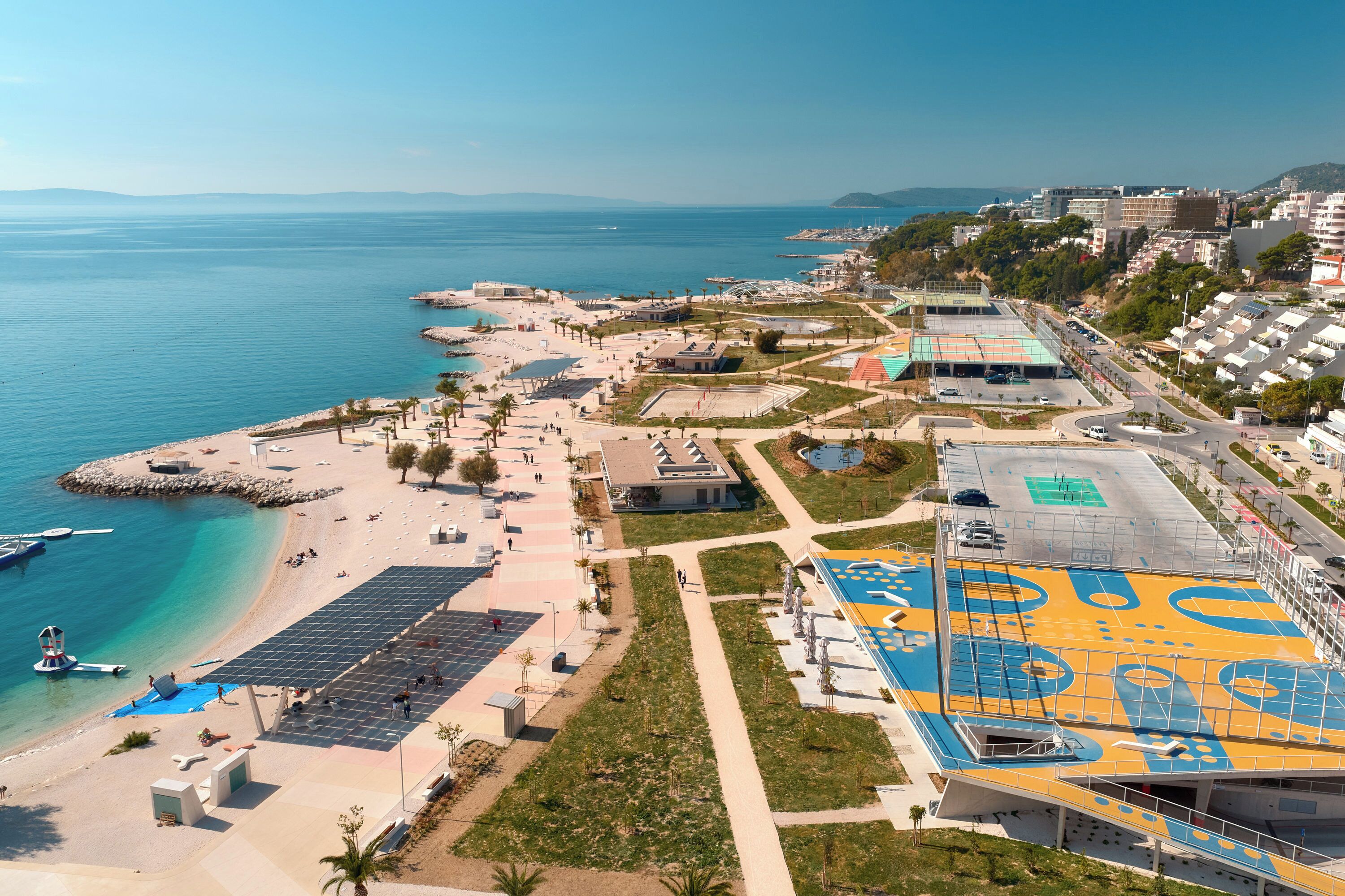 A coastal area with a beach, a sports complex, and buildings.