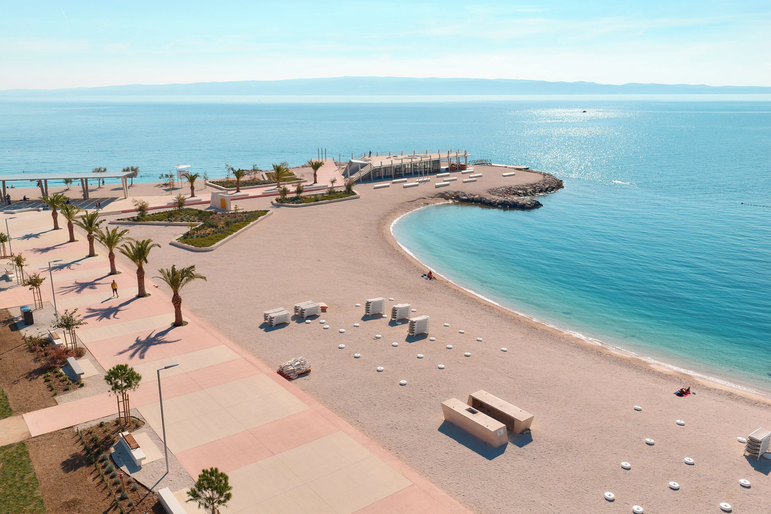 Ein Strand mit Liegestühlen, einem schattigen Bereich und Blick aufs Meer.