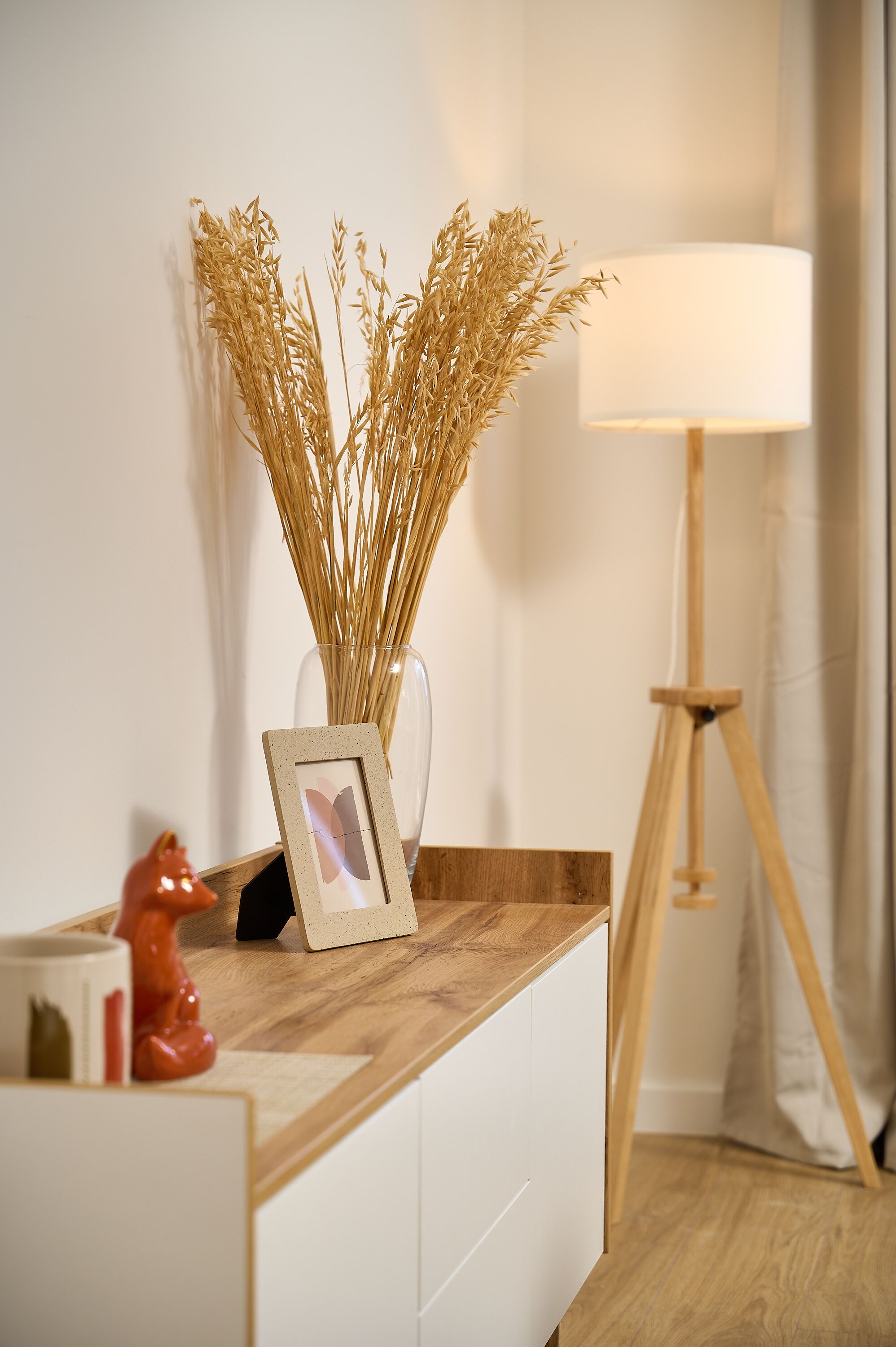 A wooden desk with a vase of dried plants, a framed picture, and a red piggy bank.