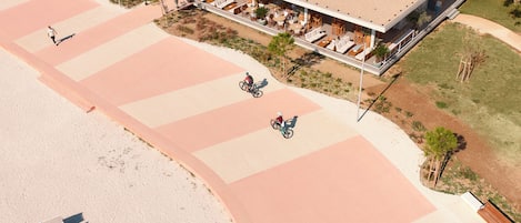 Oversigtsbillede af et badehotel med en udendørs siddeplads overdækket, en cykelsti og en sandstrand.