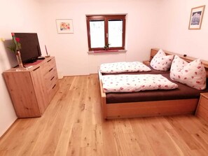 Un dormitorio con un aparador de madera, una cama con ropa de cama floral, una ventana y un televisor instalado en la pared.