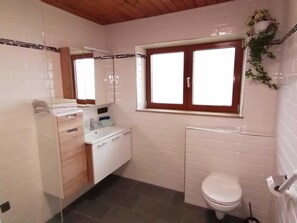 Un baño con inodoro, lavamanos con espejo y ventana.