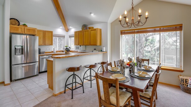 A kitchen with wooden cabinets, a stainless steel refrigerator, a dining table with chairs, and a chandelier.
