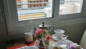 A dining table set for four with white plates, cups, and a teapot, a vase with pink flowers, and a red placemat. - Glyfada's Cosy Apartments (Glyfada)