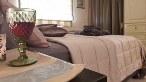 A neatly made bed with a beige comforter, a glass vase with red accents, and a patterned tray on a wooden nightstand. - Glyfada's Cosy Apartments (Glyfada)