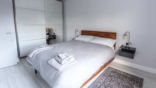 Une chambre à coucher moderne avec un grand lit, une tête de lit en bois, une table de chevet avec une lampe et une armoire.