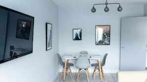 Un salon moderne avec un coin repas, comprenant une table blanche avec des chaises grises, un canapé et un grand tableau encadré accroché au mur.