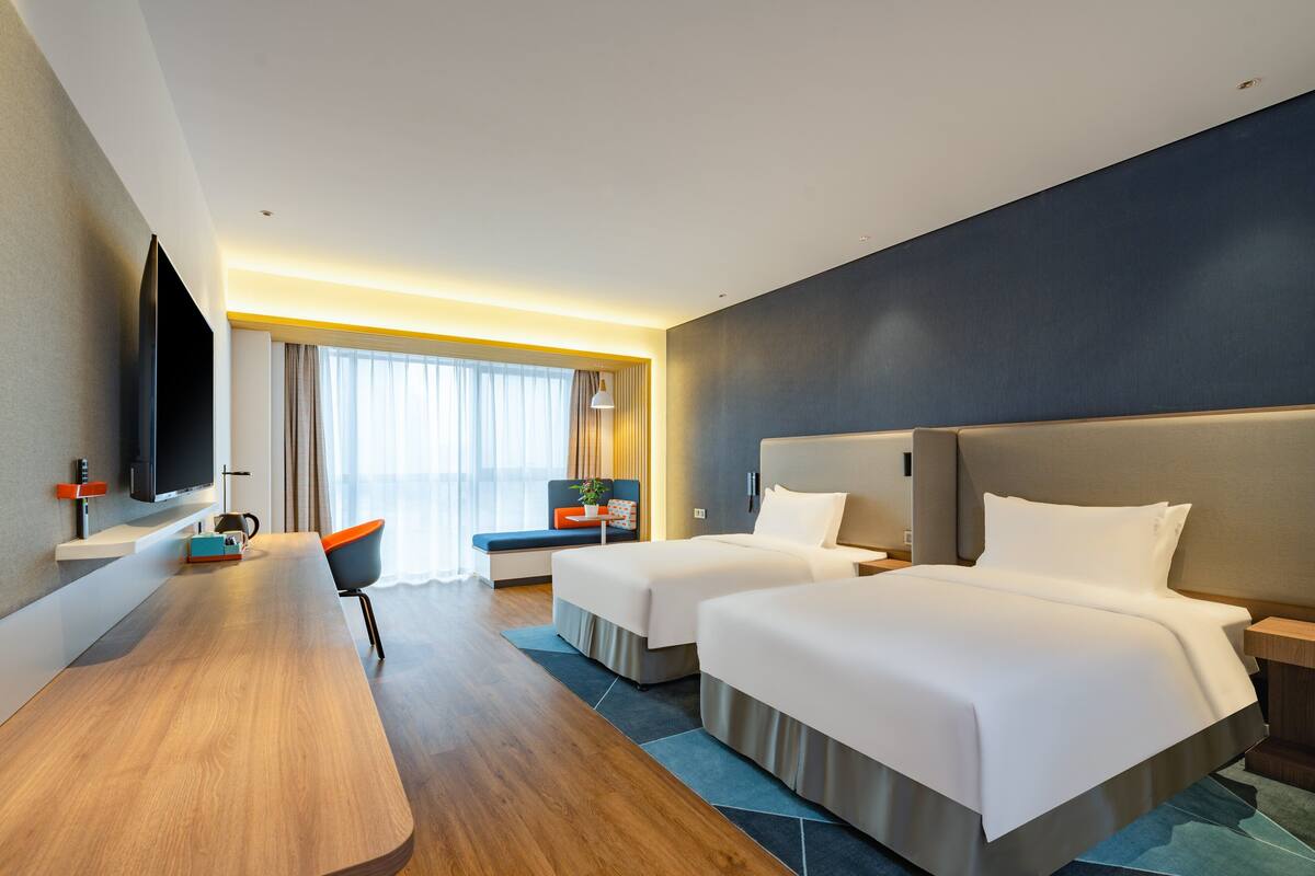 A modern hotel room with two beds, a desk, and a TV.