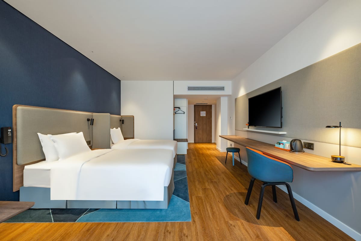 A hotel room with two beds, a desk, a chair, a TV, and a door leading to a bathroom.