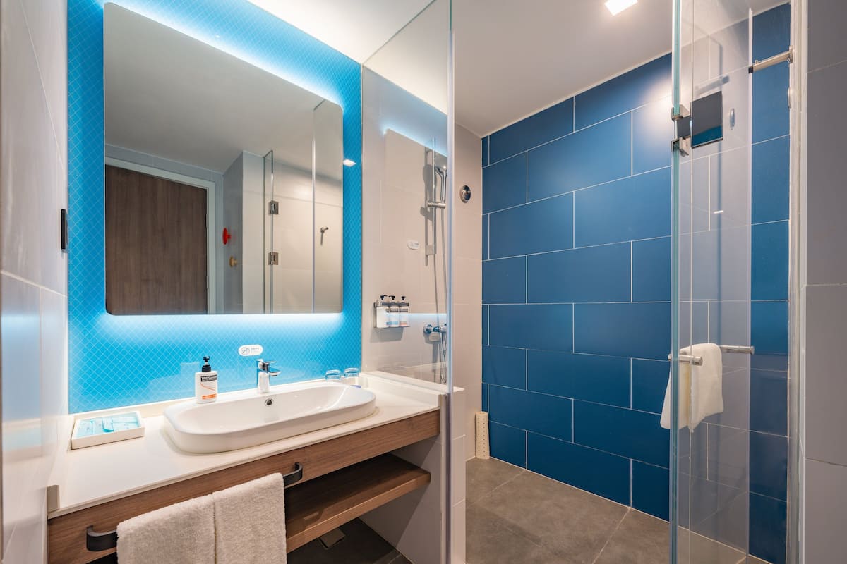 A modern bathroom with a white sink, blue tiles, and a glass shower enclosure.