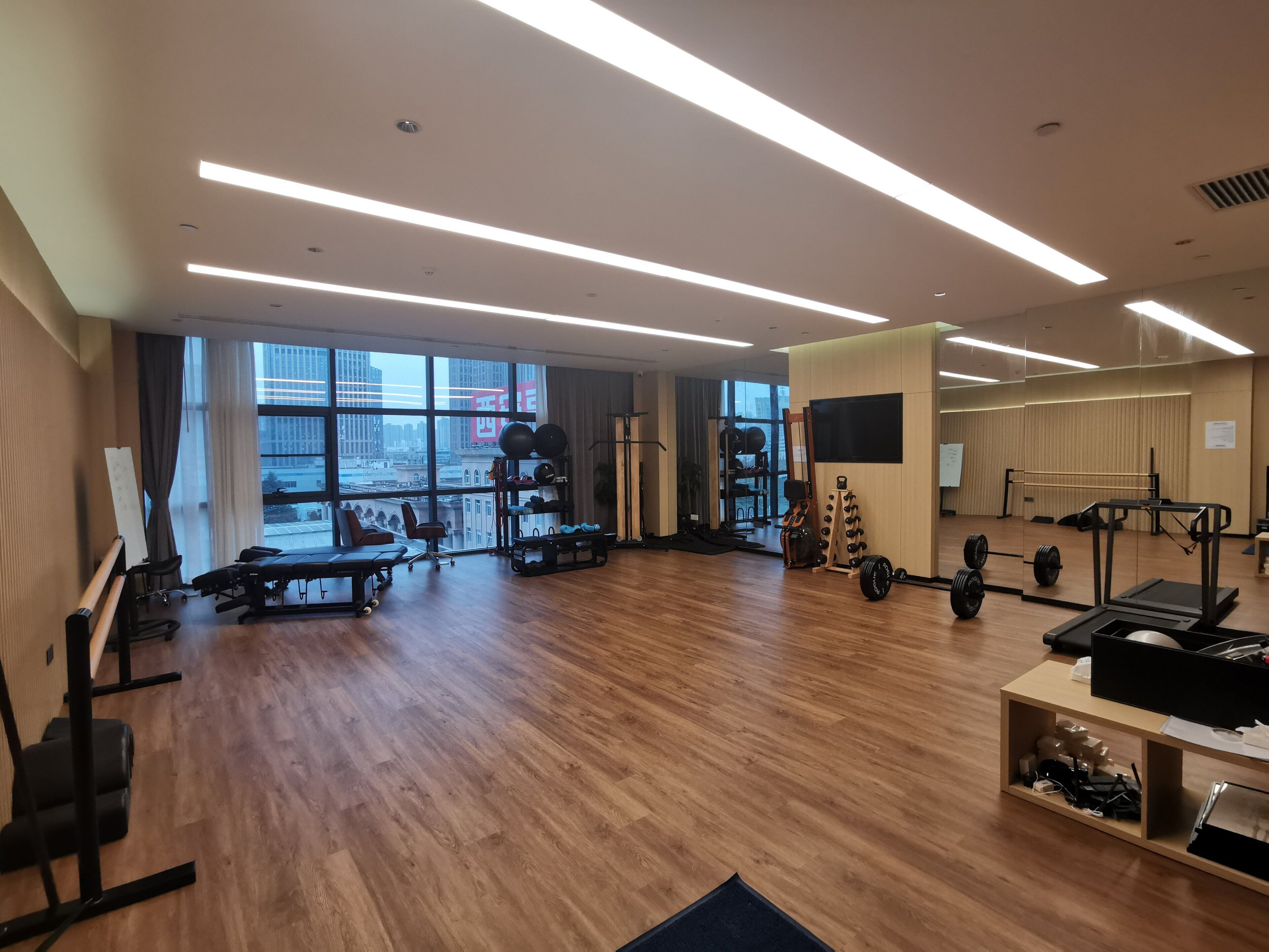 Un'ampia palestra con pavimentazione in legno, diverse attrezzature per l'allenamento, ampie finestre e vista sulla città.