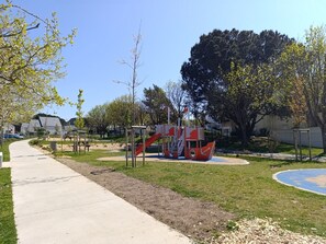 A playground with a slide and climbing structures, surrounded by grass and trees.