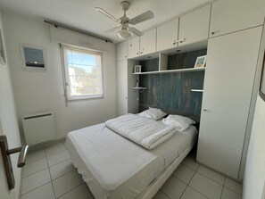 A bedroom with a bed, a ceiling fan, a window, and built-in storage cabinets.
