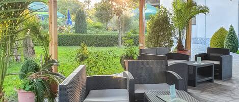 An outdoor patio with wicker furniture, potted plants, and a wooden ceiling.