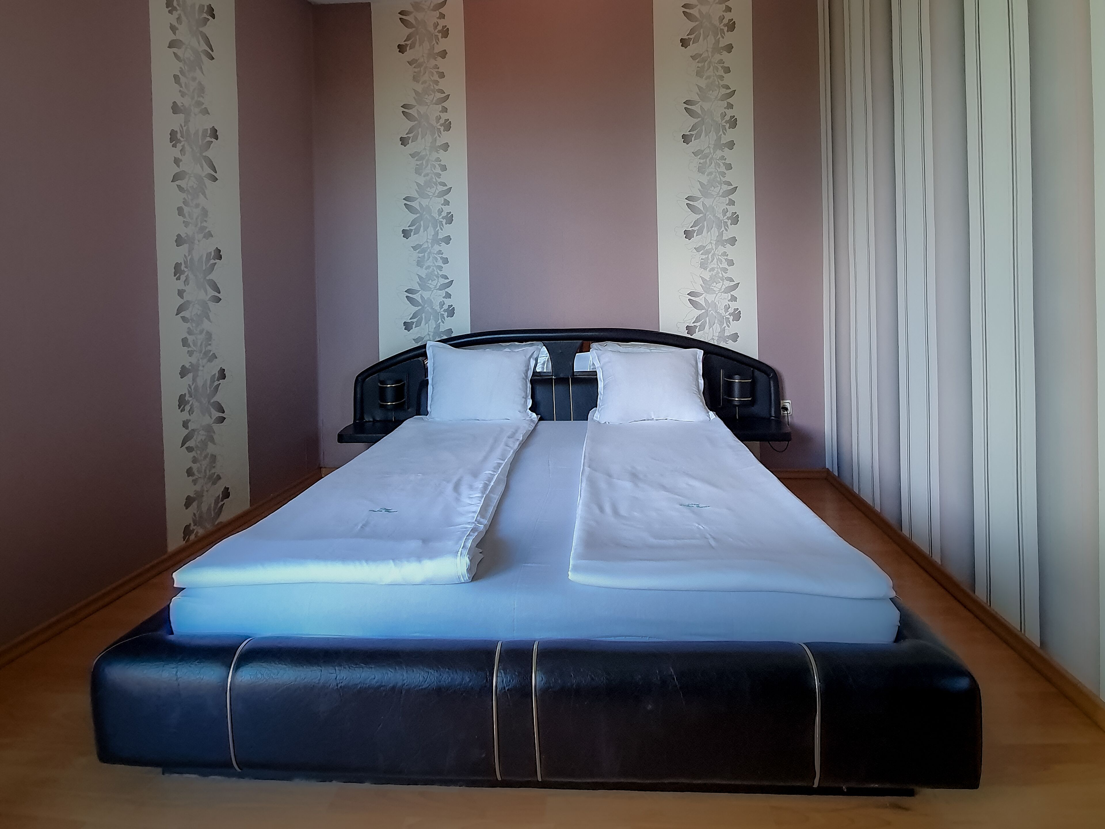 Un letto rifatto con lenzuola bianche, una testata nera e un pavimento in legno.