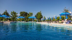 Ein klares, blaues Schwimmbecken mit blauen Sonnenschirmen, Liegestühlen und Bäumen im Hintergrund.