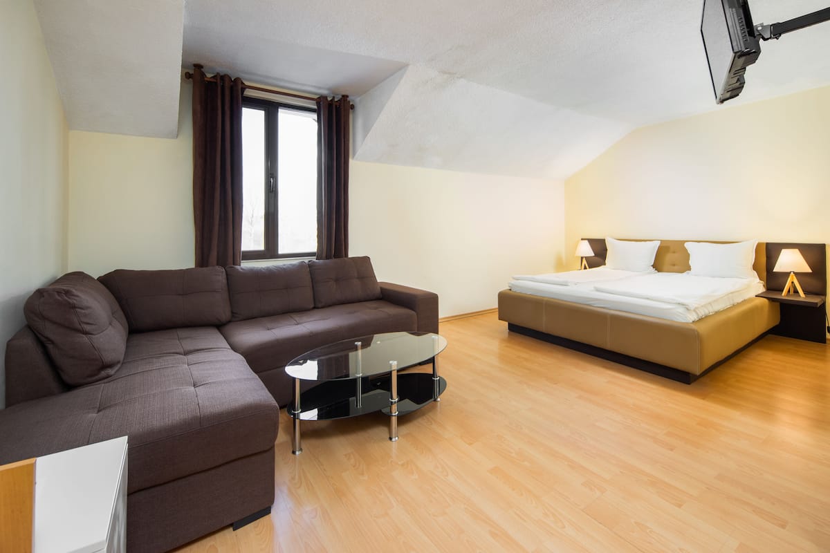 Een moderne hotelkamer met een bruine bank, een glazen salontafel, een bed met witte lakens en twee bedlampjes.