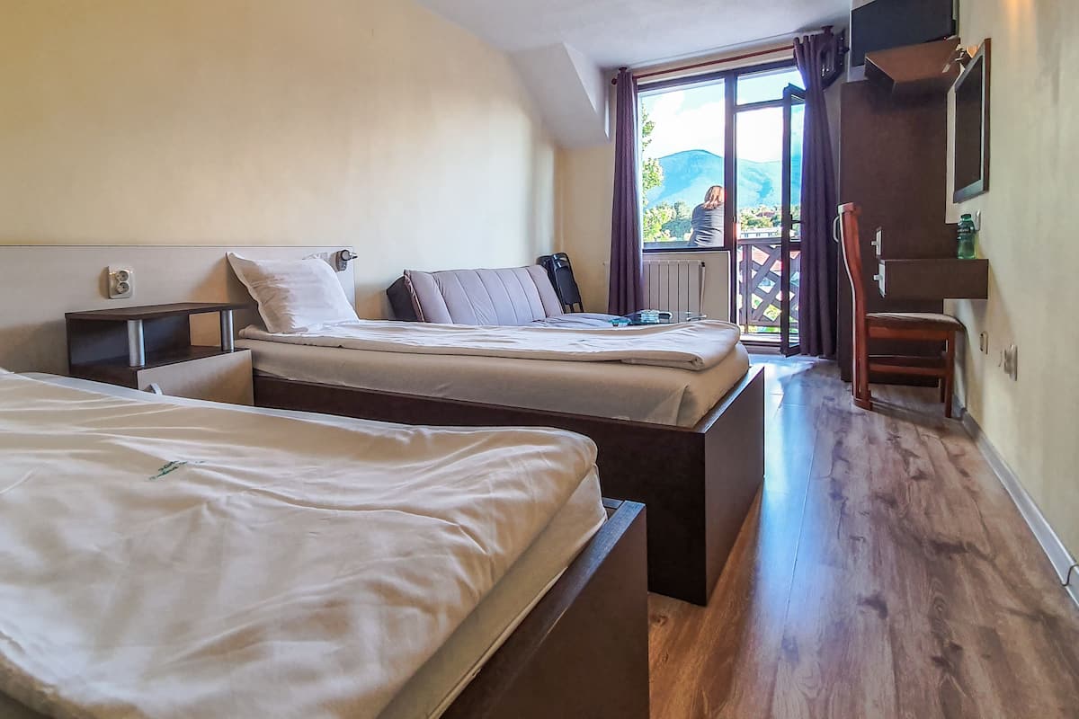 Een slaapkamer met twee bedden, een houten vloer, een raam met uitzicht op bergen en een kleine tafel met een stoel.