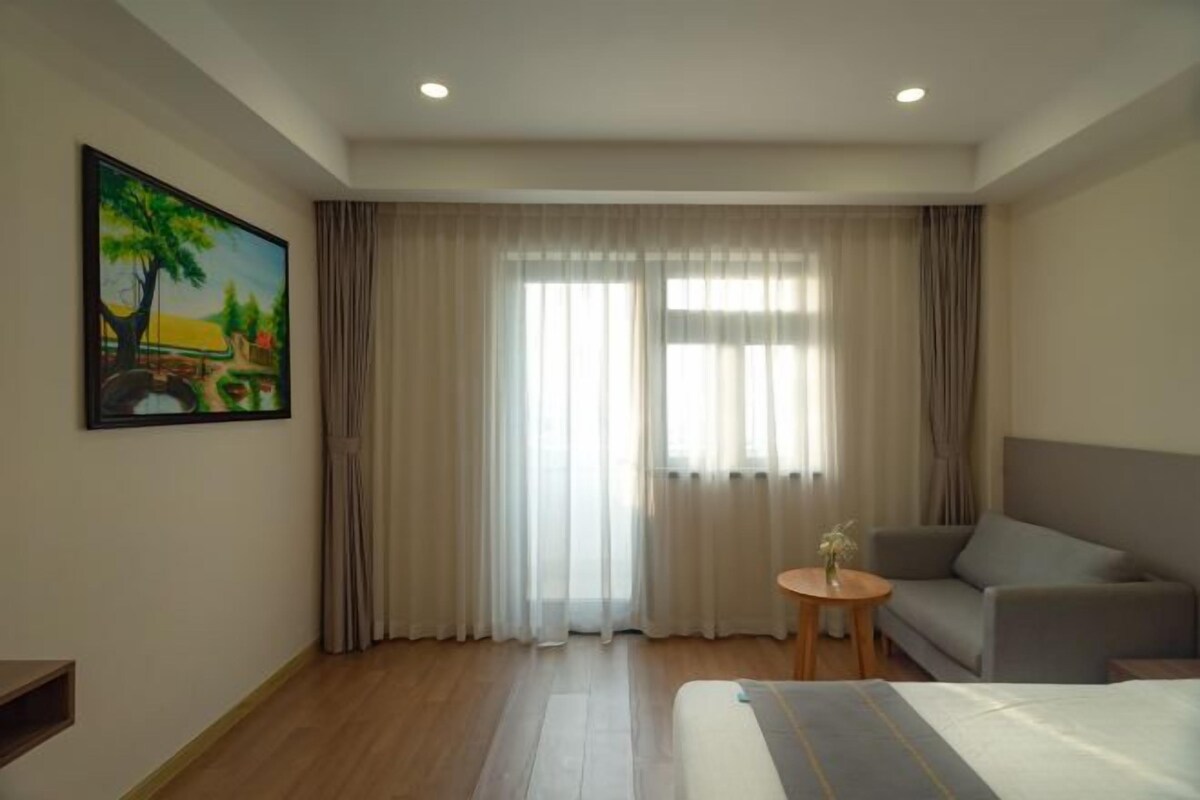 Una habitación de hotel con una cama, un sofá, una mesita con un florero y un cuadro en la pared.