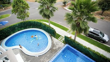 Una piscina residenziale dalla forma sinuosa, circondata da un prato curato e palme.