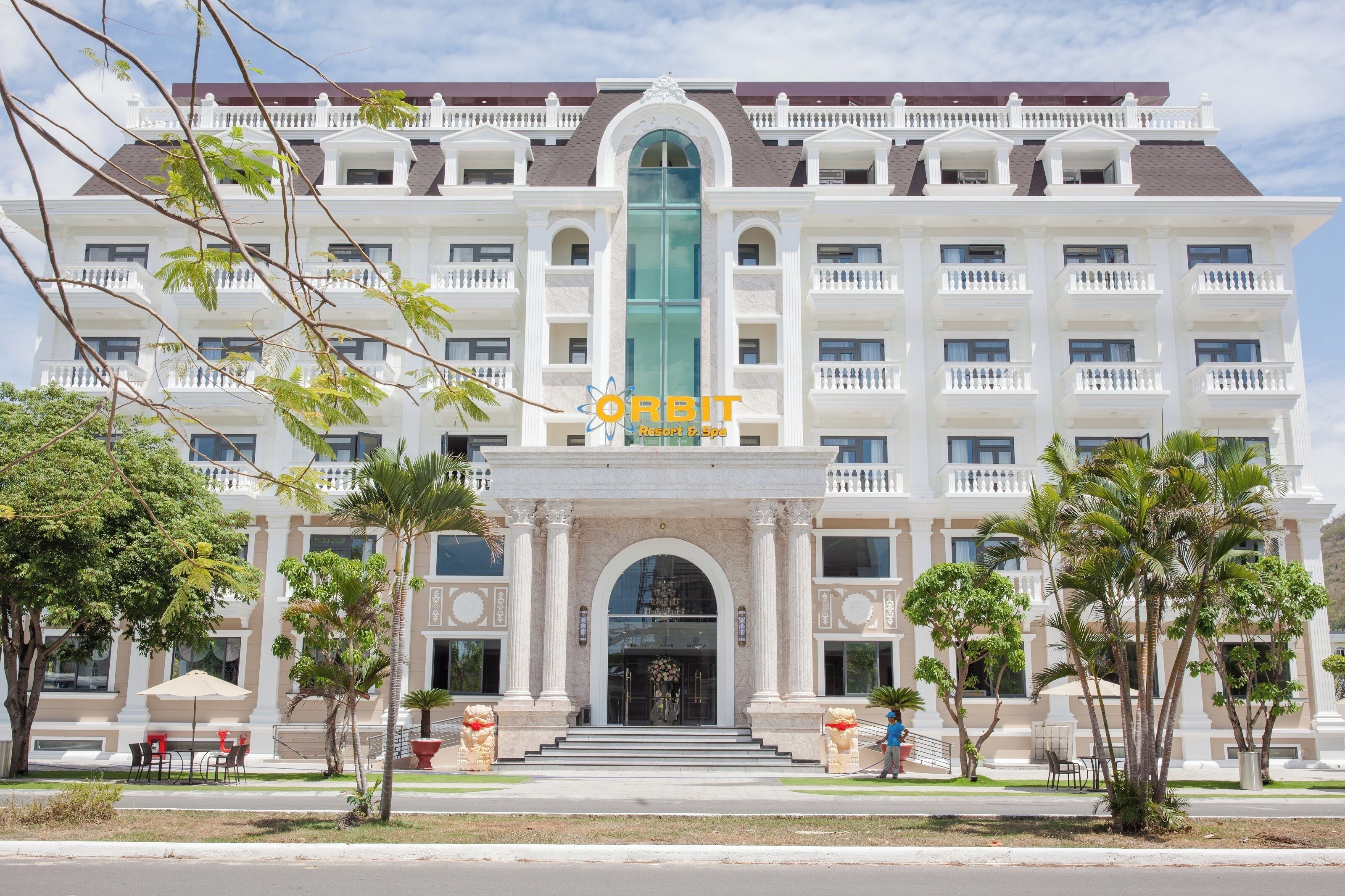 A large, multi-story hotel with a central entrance, surrounded by palm trees and outdoor seating.