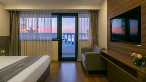 Habitación de hotel con cama, sofá, televisión y balcón con vista al atardecer.