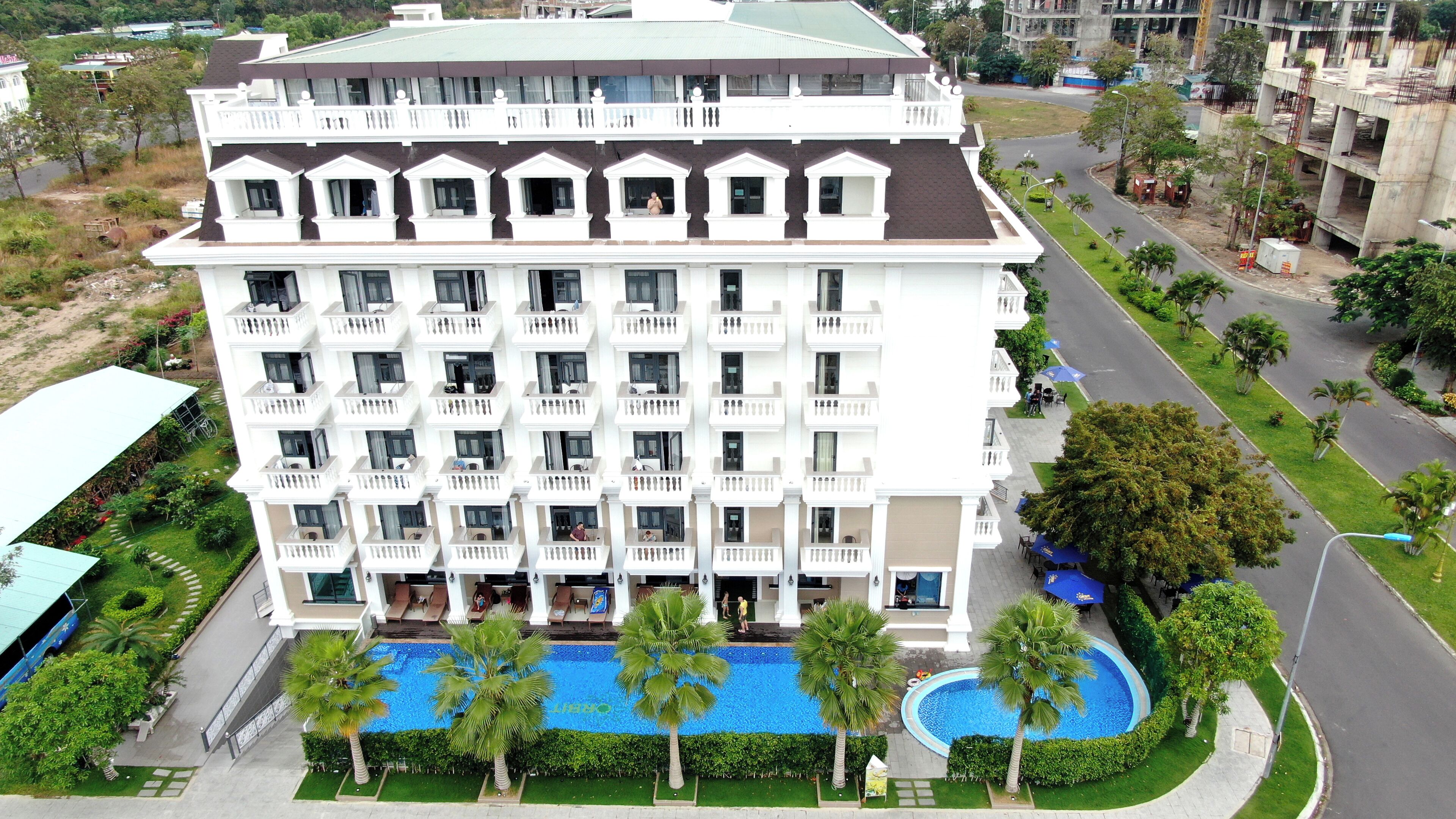A multi-story hotel with balconies, a swimming pool, and a landscaped garden.
