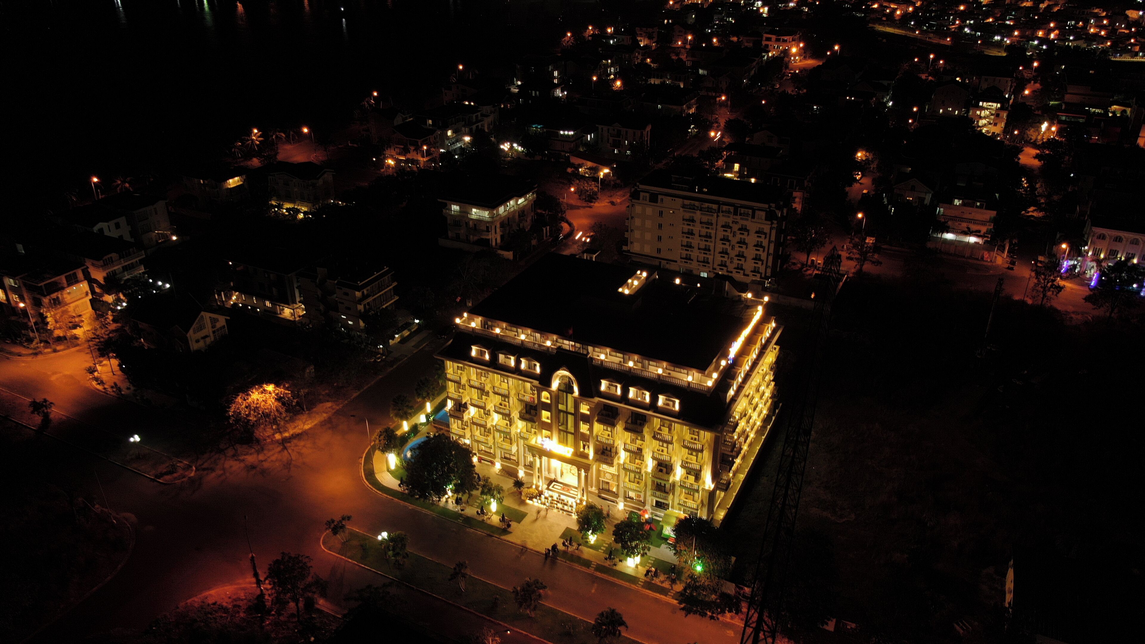 Luchtbeeld van een hotel met een centrale binnenplaats, omgeven door een dichtbebouwd stedelijk gebied 's nachts.