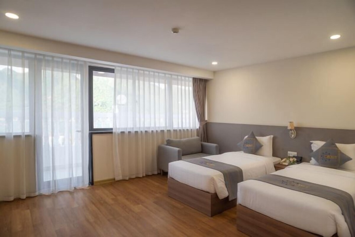 A hotel room with two beds, a sofa, and a large window with sheer curtains.