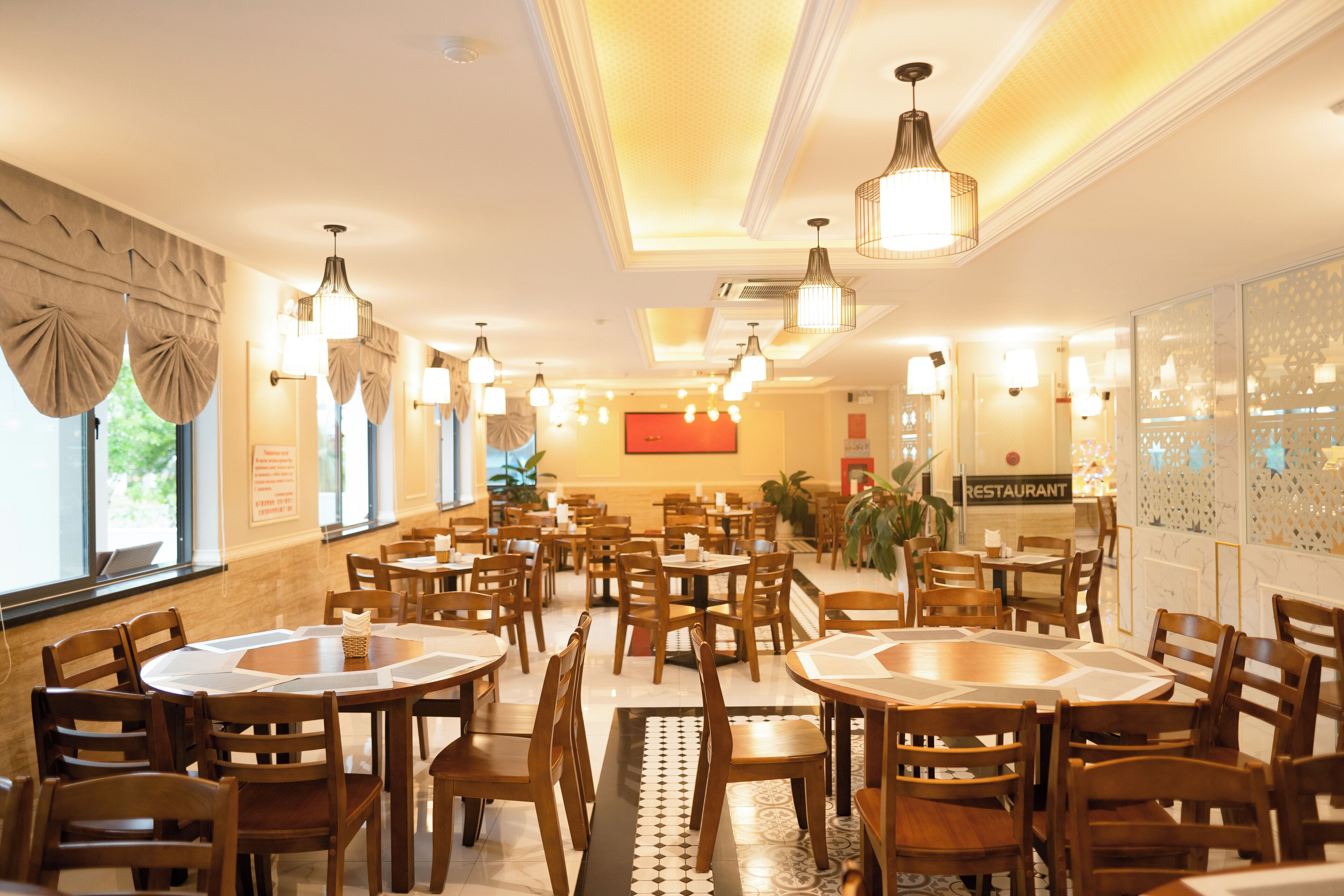 Un restaurant spacieux, doté de nombreuses tables et chaises, d’un éclairage chaleureux et d’une enseigne bien visible indiquant qu’il s’agit d’un restaurant.