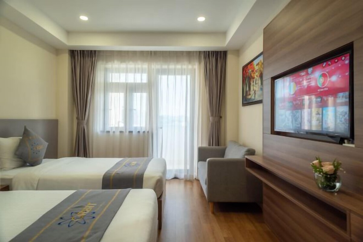 A hotel room with two beds, a sofa, a TV mounted on the wall, and a wooden cabinet.