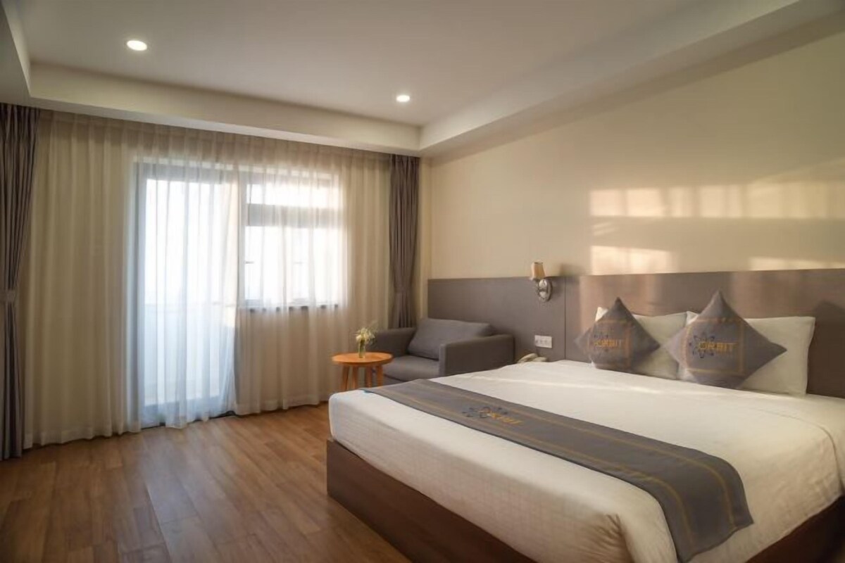 A hotel room with a large bed, a sofa, a small table, and a window with curtains.