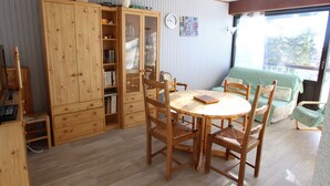 A cozy room with a wooden dining table and chairs, a green sofa, and a wooden cabinet with glass doors. - Beautiful 2-room apartment at the foot of the slopes in Chamrousse (Chamrousse)