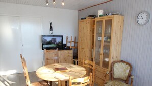 A dining area with a round wooden table, four chairs, a cabinet with glass doors, a television, and a clock on the wall. - Beautiful 2-room apartment at the foot of the slopes in Chamrousse (Chamrousse)