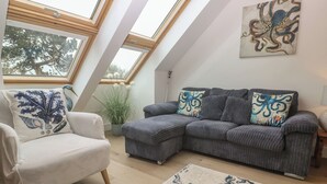 A loft-style living room with a sectional sofa, a single armchair, a large window, and a ceiling fan. - Upper Deck (Truro)