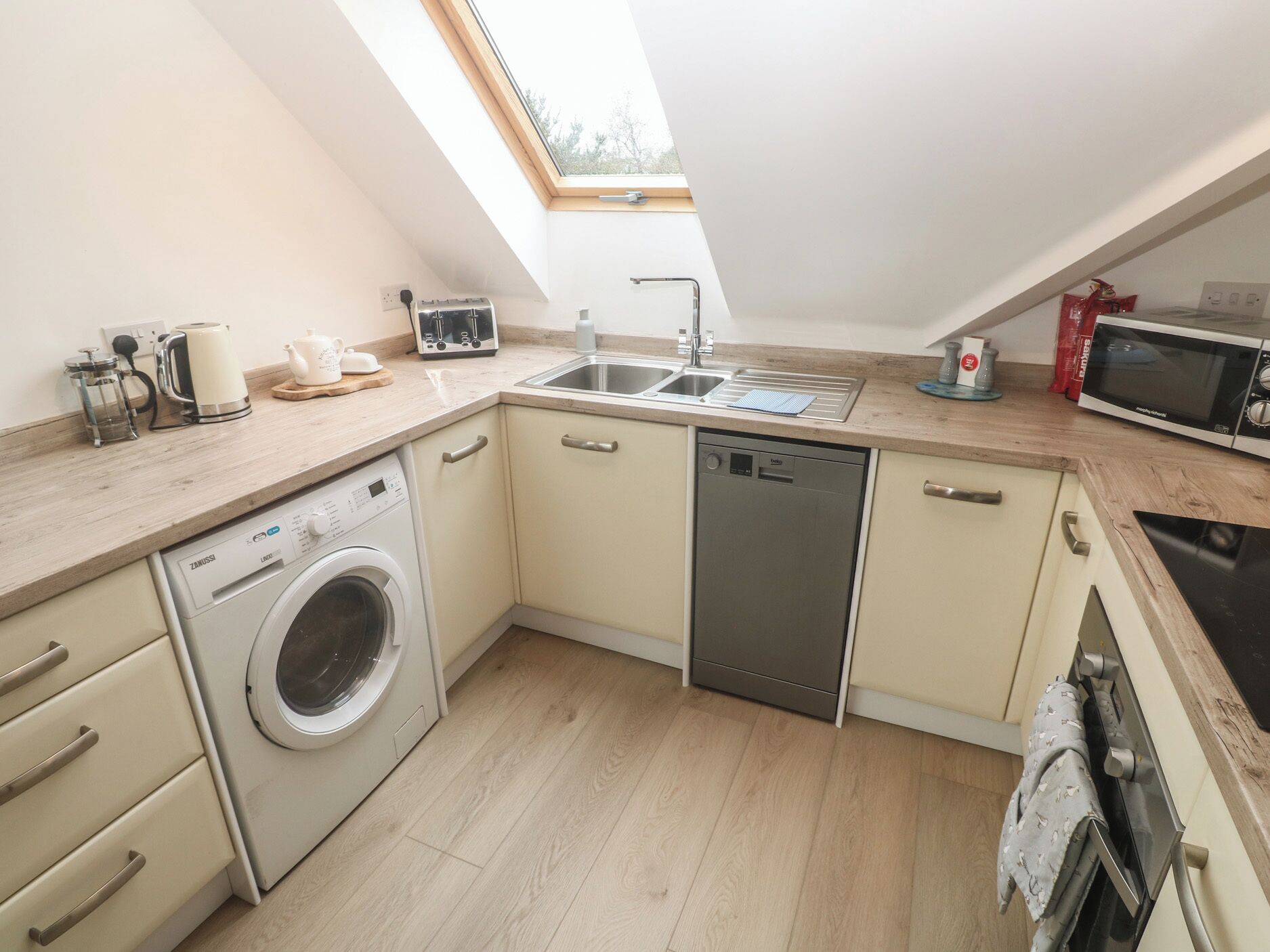 A compact kitchen with a washing machine, dishwasher, microwave, and a skylight.