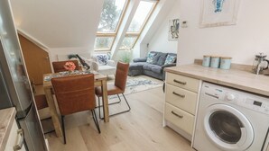 A modern kitchen with a built-in washing machine, a dining area with a table and chairs, and a living space with a sofa and a coffee table. - Upper Deck (Truro)