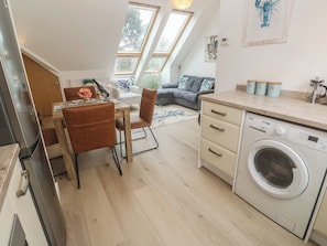 A modern kitchen with a built-in washing machine, a dining area with a table and chairs, and a living space with a sofa and a coffee table. - Upper Deck (Truro)