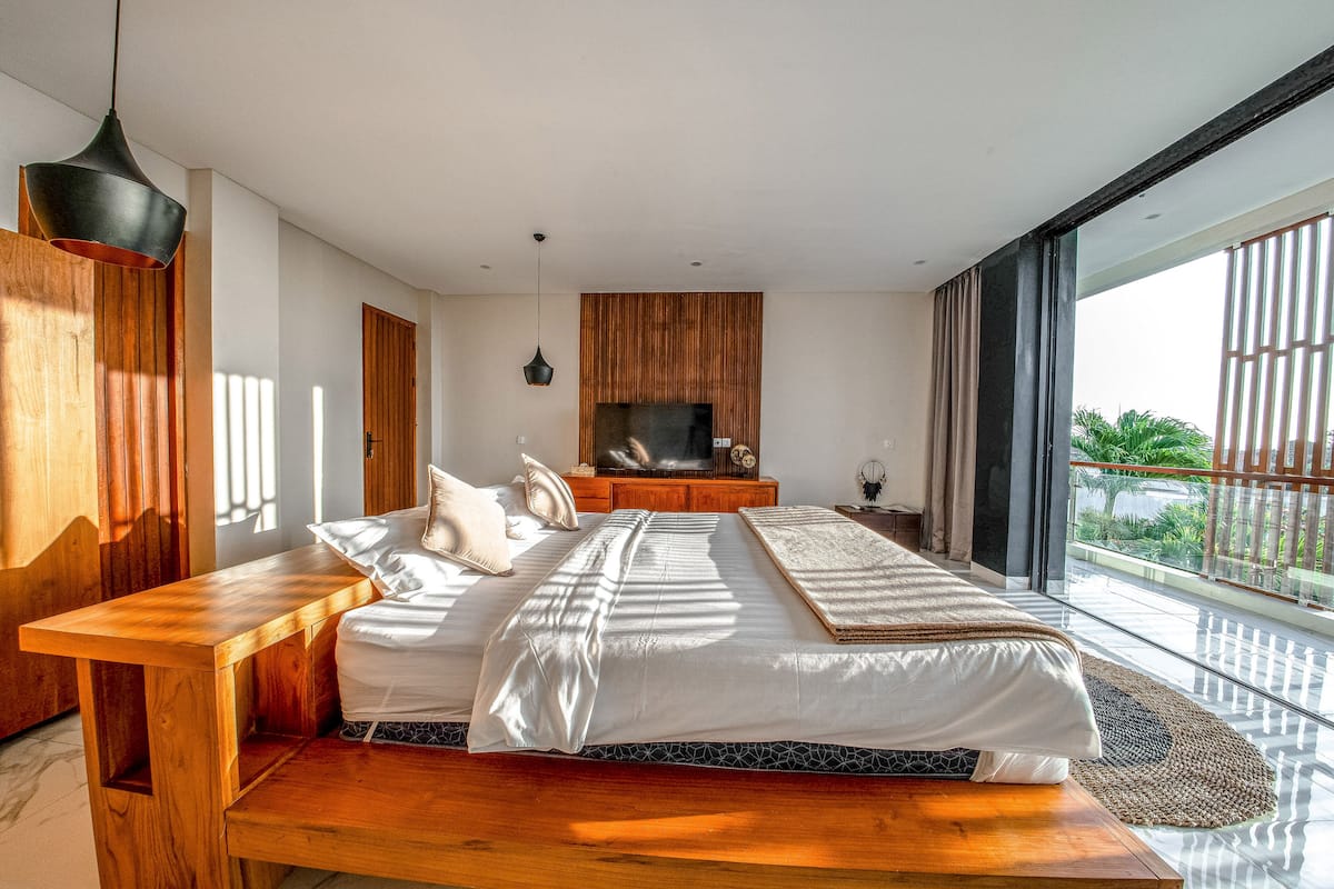 Ein modernes Schlafzimmer mit einem großen Bett, Holzmöbeln, einem Fernseher und Balkonblick.