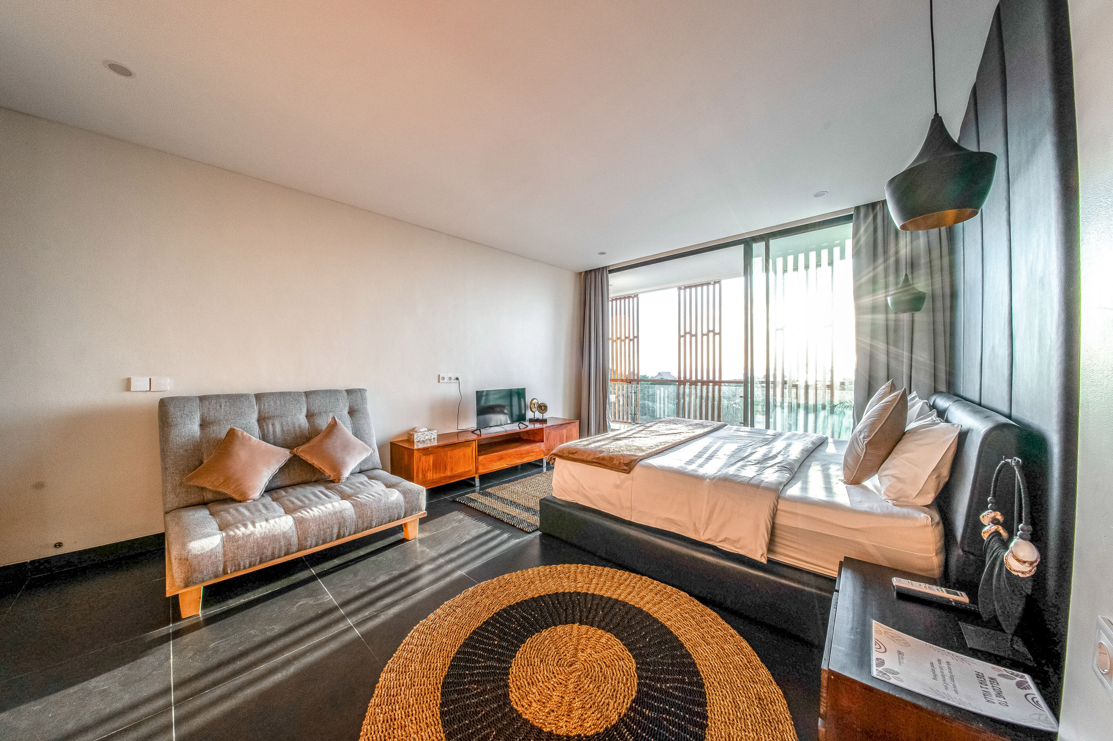 A modern bedroom with a sofa, a bed, a TV, and a large window.