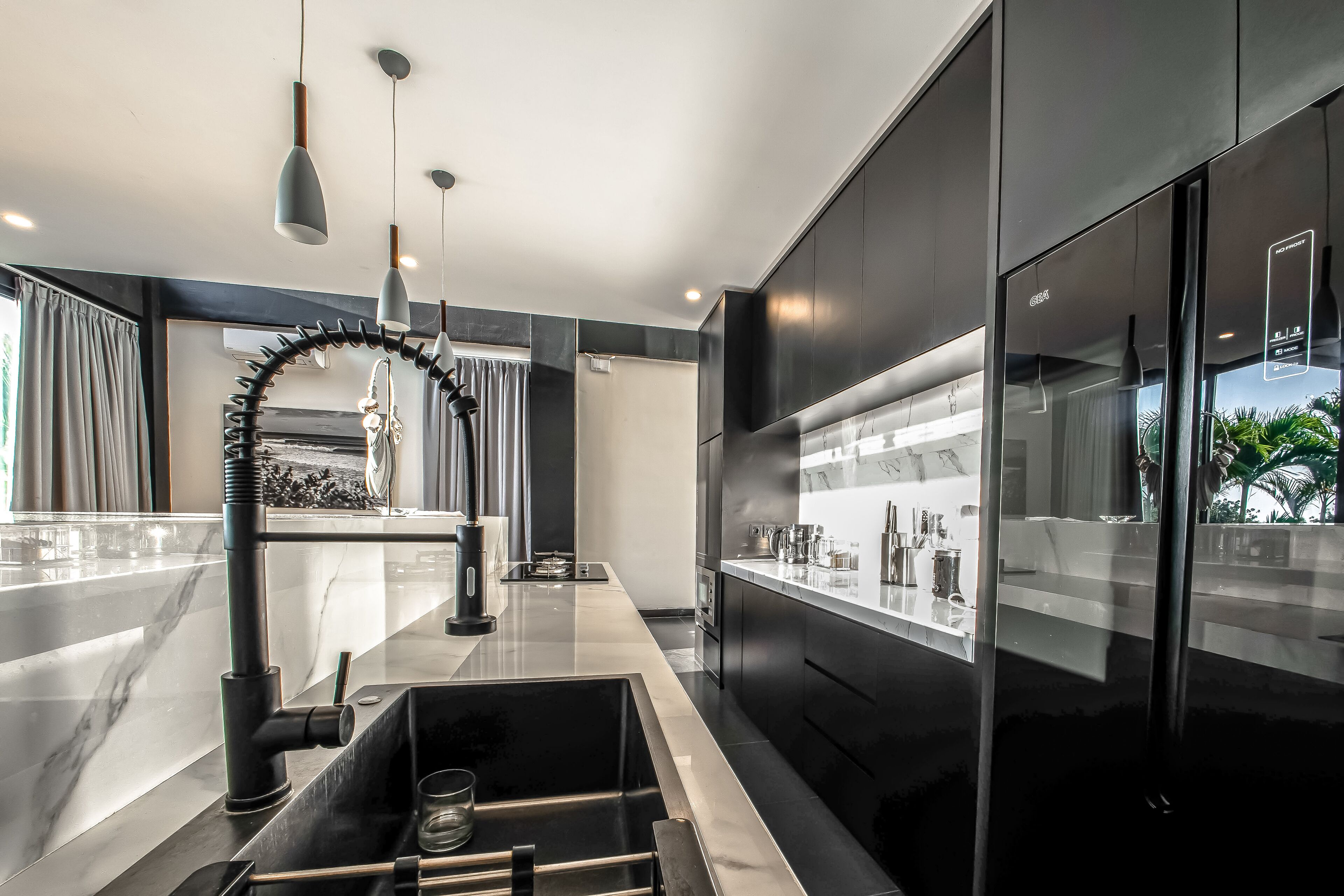 A modern kitchen with sleek black cabinets, a stainless steel sink, and pendant lighting.