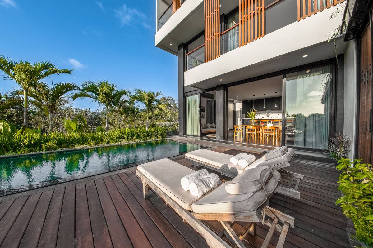 Ein modernes Haus mit Pool, Liegestühlen und Essbereich.