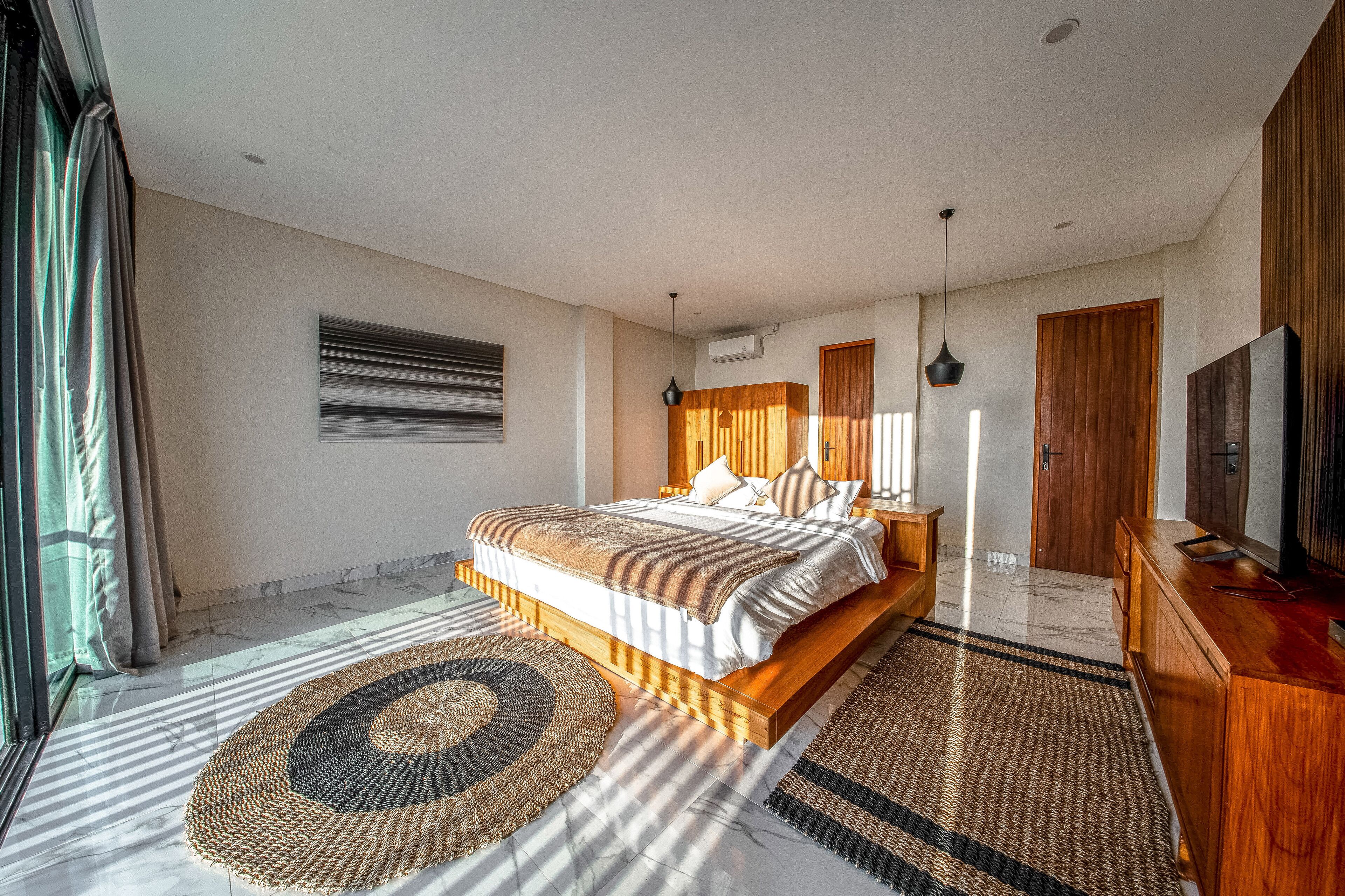 Une chambre moderne avec un grand lit, une tête de lit en bois et un téléviseur posé sur une commode en bois.
