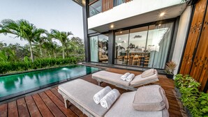 Un área de piscina moderna al aire libre con sillones de descanso y una terraza de madera.