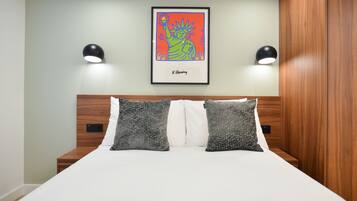 Cama bem arrumada com duas almofadas estampadas, uma obra de arte emoldurada acima e duas luminárias na parede.