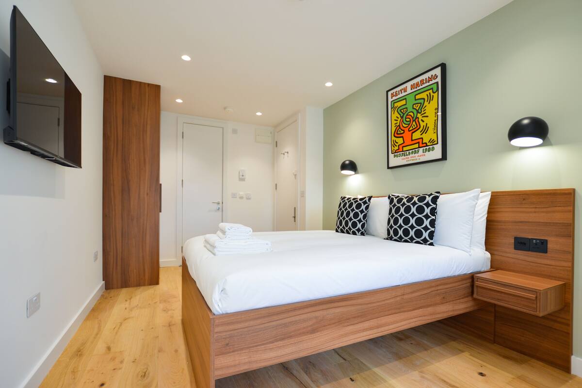 A modern bedroom with a wooden bed, white linens, and a wall-mounted TV.