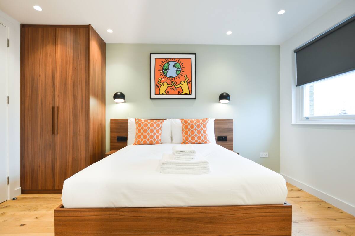 A modern bedroom with a wooden bed frame, a large wardrobe, and a framed artwork on the wall.