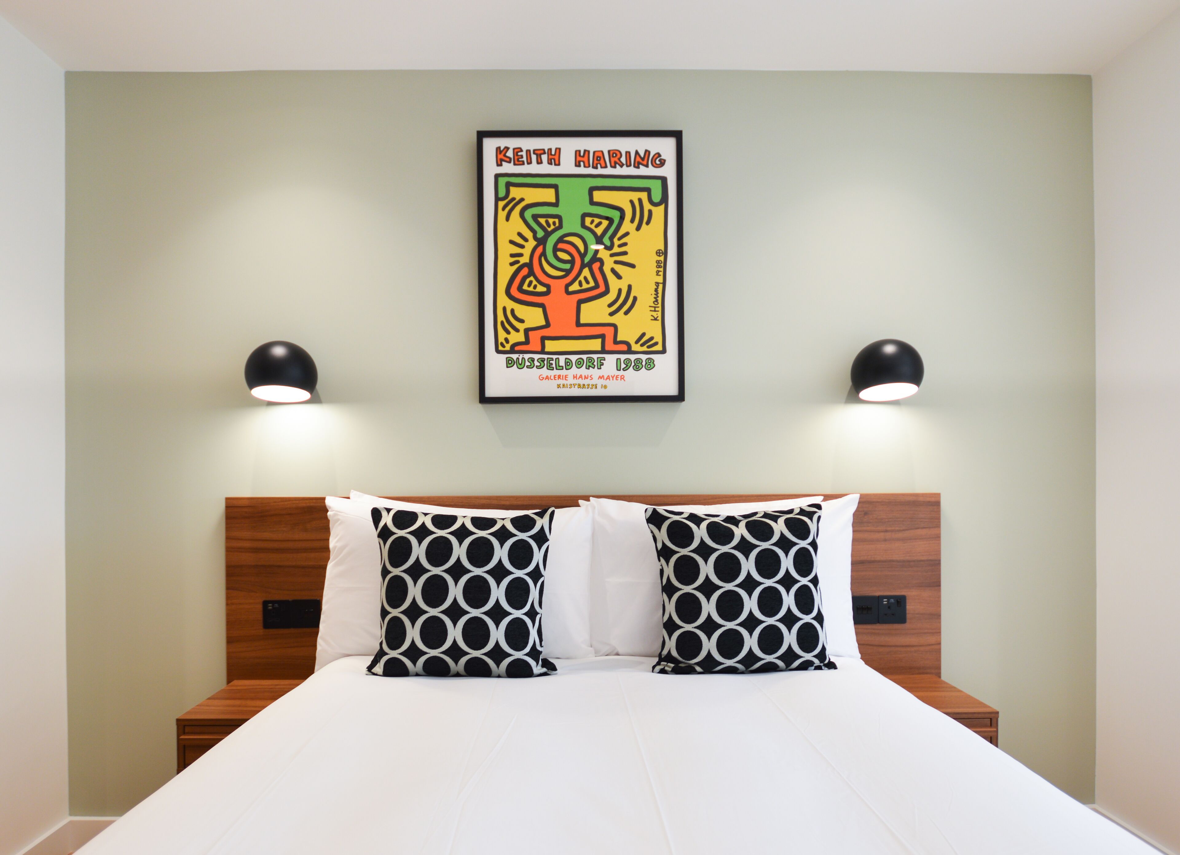 A hotel room with a bed, two black lamps, and a framed artwork on the wall.